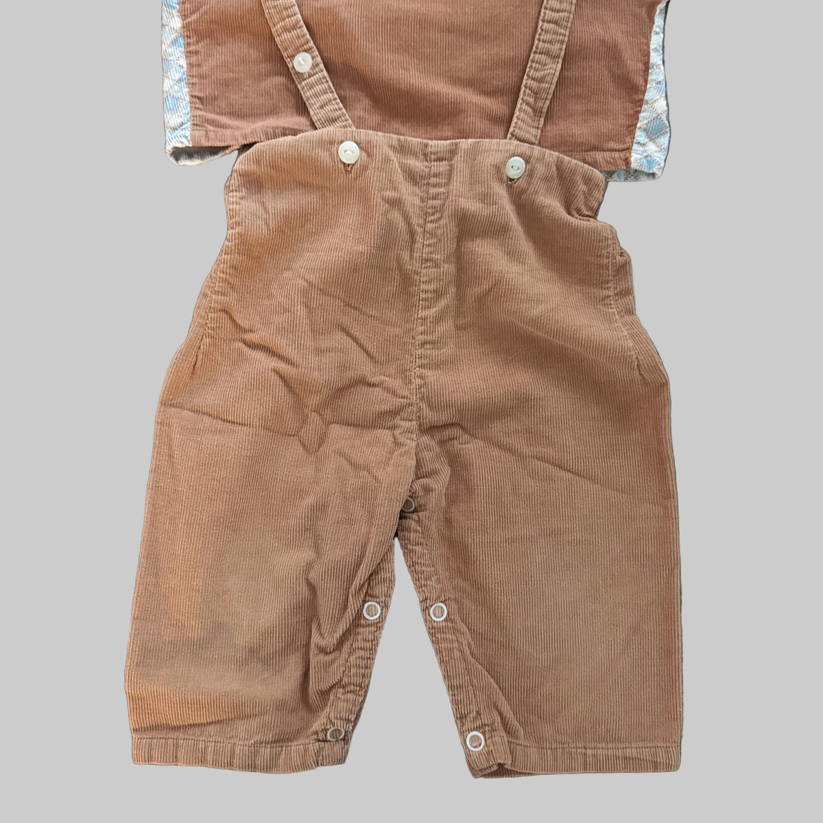 A pair of toddler boy's corduroy bib overalls in a warm brownish-tan color, laid flat on a textured gray fabric background.