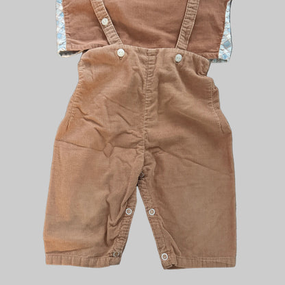 A pair of toddler boy's corduroy bib overalls in a warm brownish-tan color, laid flat on a textured gray fabric background.