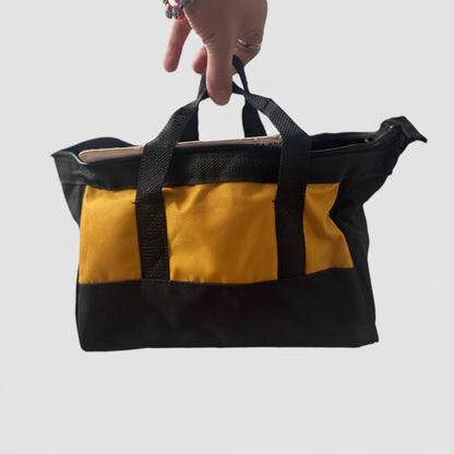 A black and mustard yellow canvas tote bag being held by a hand in an indoor setting with a blurred background.
