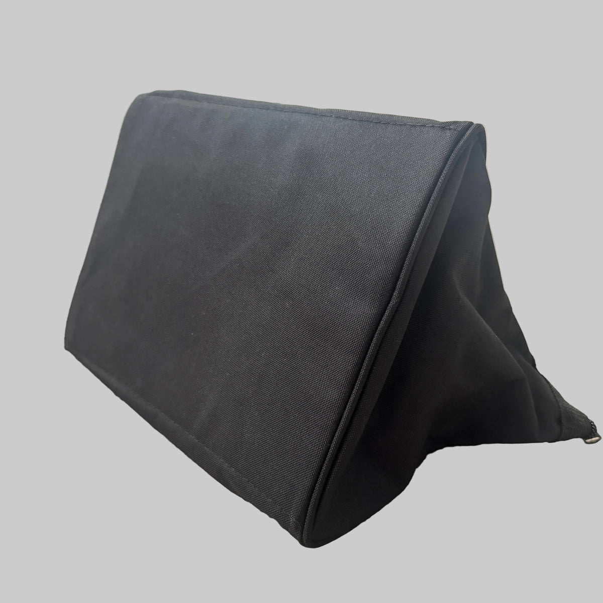A black triangular wedge-shaped stand made of canvas or fabric, resting on a beige carpeted floor in an indoor setting.