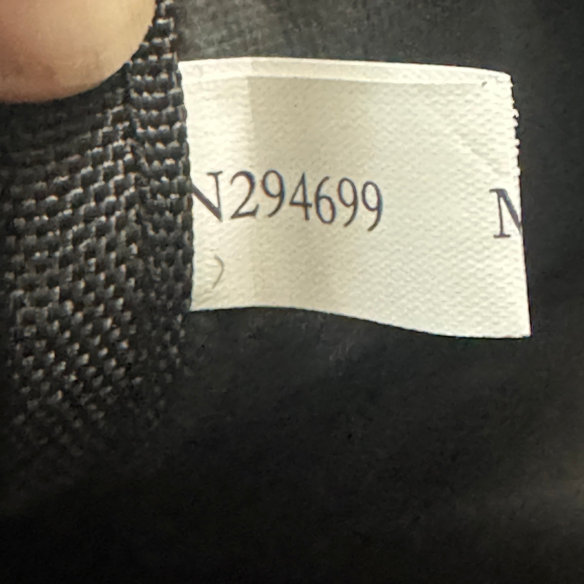 Close-up of a garment's interior neck label showing the printed number N294699 on a white paper tag, next to black knit fabric.