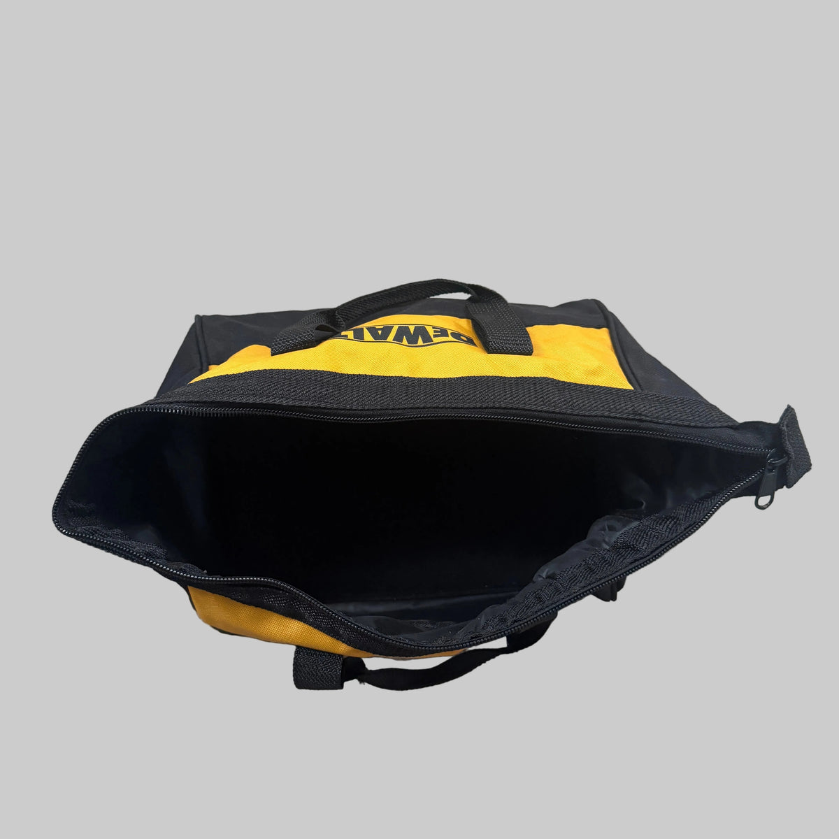 A black and yellow DeWalt utility bag shown open from above, placed on a gray carpeted floor. The DeWalt logo is visible in yellow on the black upper panel.