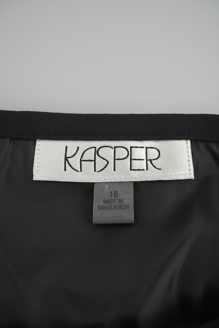 Close-up of a KASPER garment interior showing a white brand label stitched onto a black satin-like lining, with a gray textured fabric at the top and a small size tag reading 18 made in Bangladesh.