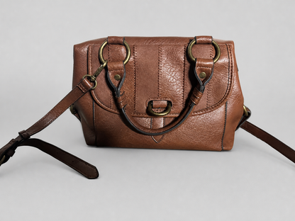 A brown textured leather handbag with a structured rectangular shape, featuring a front flap, brass-tone hardware, a top handle, and a detachable shoulder strap, photographed against a neutral light gray background.