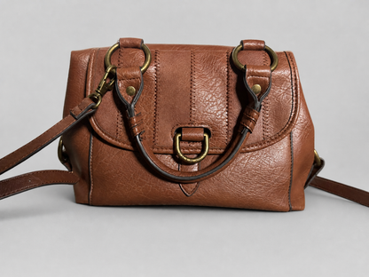 A brown textured leather handbag with a flap front, brass-tone hardware, and a shoulder strap, photographed on a light gray studio background.