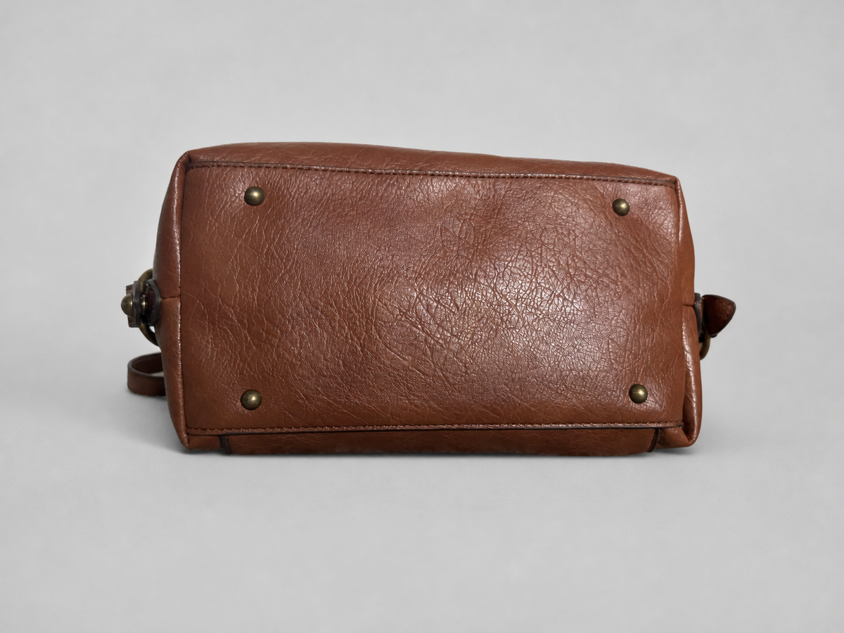A brown leather shoulder bag shown from the back, featuring a textured leather finish, brass-toned rivets, and a small strap loop on a light gray background.