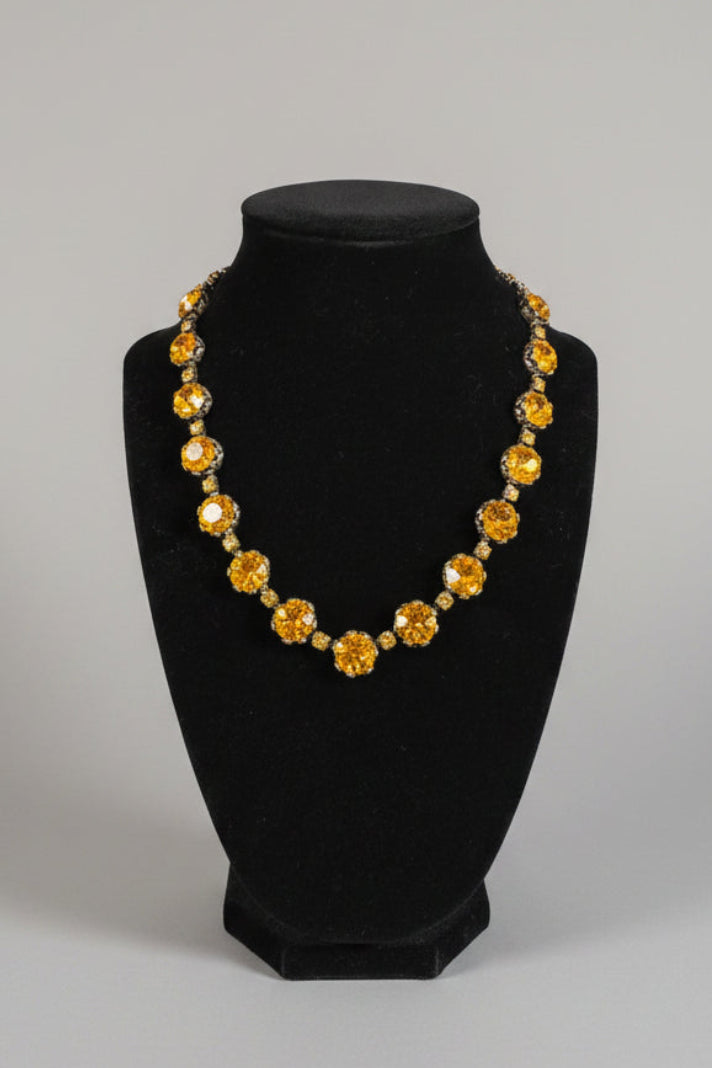 A gold-tone statement necklace with large round amber-yellow crystals, displayed on a black velvet jewelry bust.