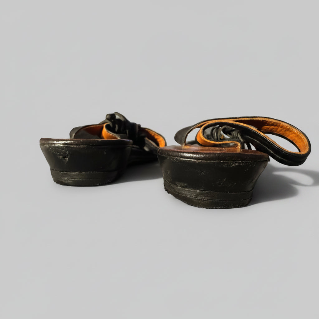 A pair of black leather boot heels or heel inserts with orange-brown lining, resting on a textured gray blanket in a home setting.