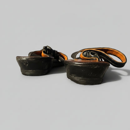 A pair of black leather boot heels or heel inserts with orange-brown lining, resting on a textured gray blanket in a home setting.