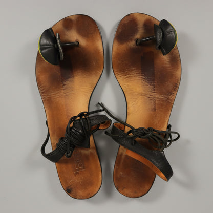 A pair of vintage B&B brand leather slide sandals with black straps and toe caps, laid flat on a textured gray surface in direct sunlight.