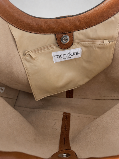 Close-up of a beige tote bag interior showing a zippered pocket with a white label reading mandarin, tan leather trim, and a metal snap closure.