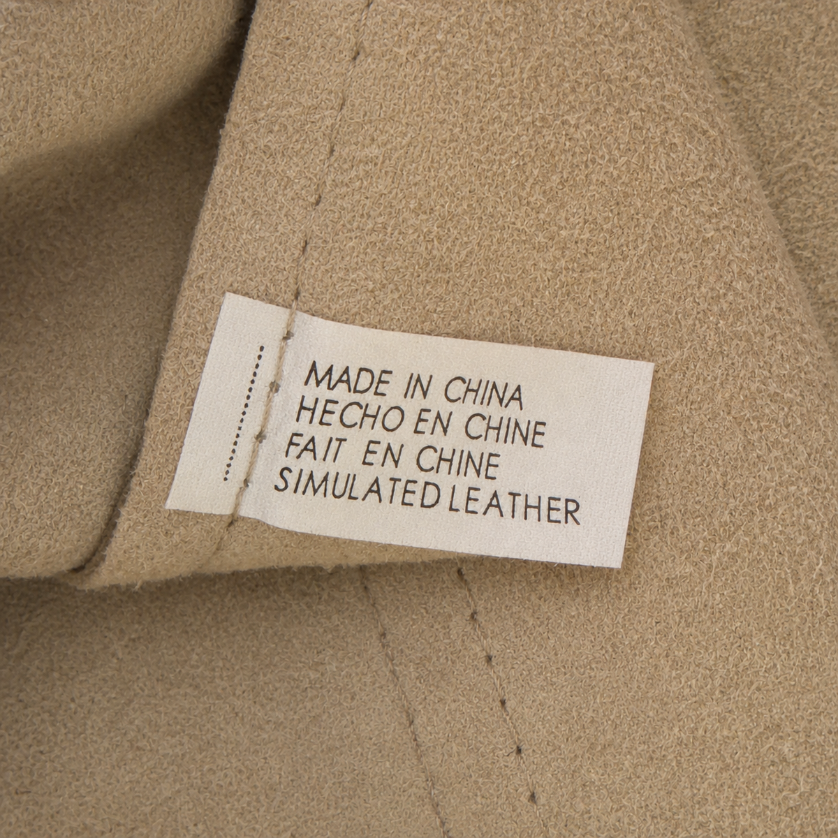 Close-up of a beige fabric garment with a sewn-on fabric label that reads 'MADE IN CHINA HECHO EN CHINE FAIT EN CHINE SIMULATED LEATHER'.