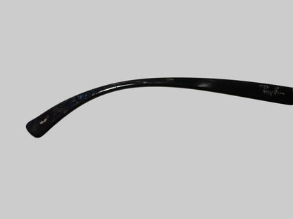 A close-up of a single black eyeglass arm resting on a white textured surface, with part of a hand holding the other half of the glasses visible at the lower left.
