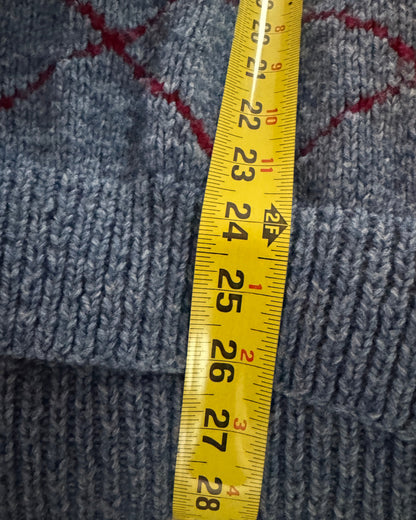 A close-up of a blue knit fabric with a red diamond pattern, shown with a yellow tape measure to indicate the size of the item.
