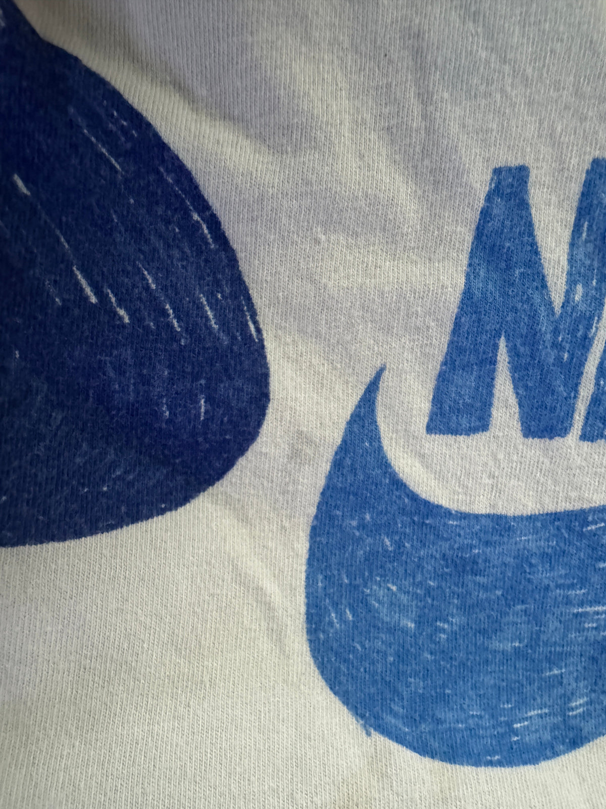 Close-up of a white or off-white fabric surface with a large blue graphic print, showing part of a bold blue letter and a dark blue textured shape.