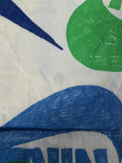 Close-up of a white fabric surface with a partial abstract print in blue and green, showing knit texture and stitching.