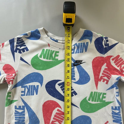 A white Nike crewneck sweatshirt featuring a colorful all-over print of blue, green, and red swooshes and logos, shown with a yellow tape measure laid vertically down the center on a gray textured fabric background.