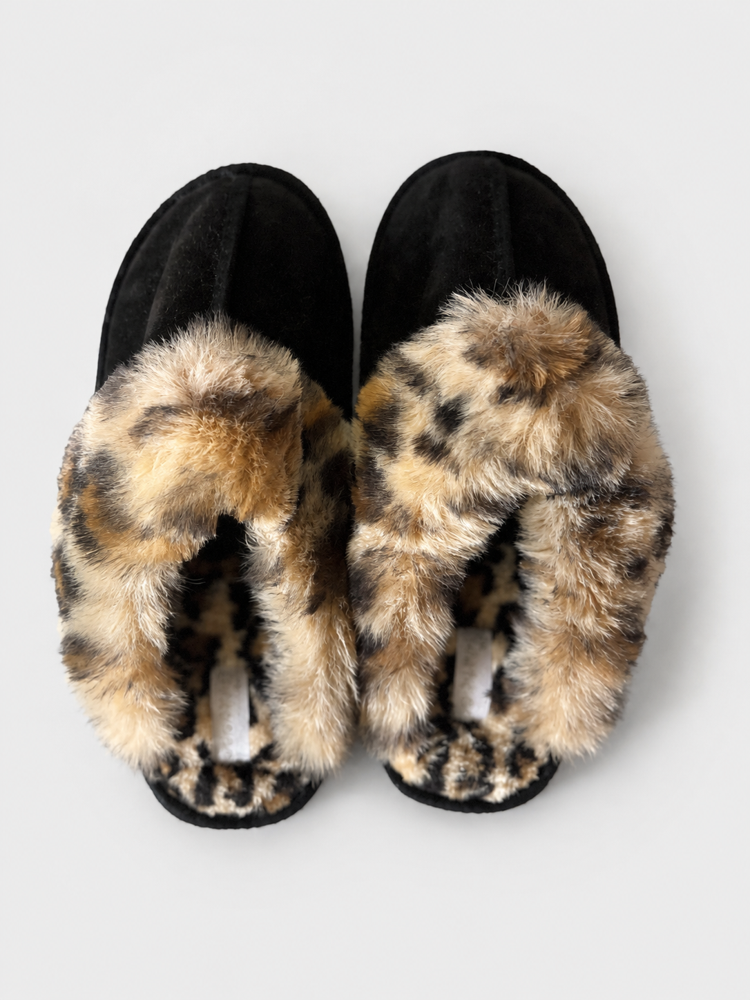 A pair of black slipper-style slippers with plush leopard-print faux fur trim, photographed from above on a light gray background.