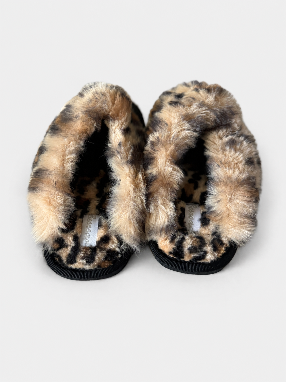 A pair of plush leopard-print slippers with black ribbed soles, photographed from a top-down view on a light gray background.