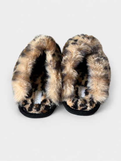 A pair of plush leopard-print slippers with black ribbed soles, photographed from a top-down view on a light gray background.
