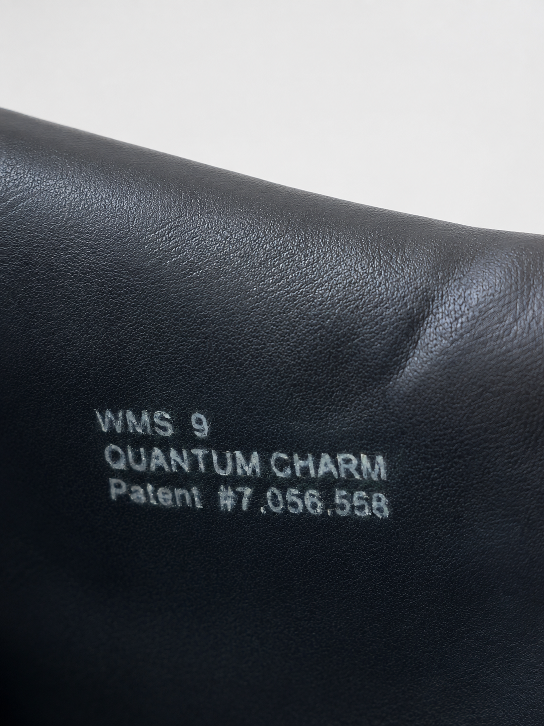 Close-up of a black leather surface with white printed text reading 'WMS 9 QUANTUM CHARM Patent #7,056,558' on a light gray background.