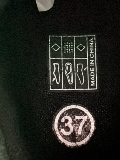 Close-up of a black shoe interior label showing a circular size stamp with the number 37 and a square 'MADE IN CHINA' compliance patch with shoe silhouette icons.