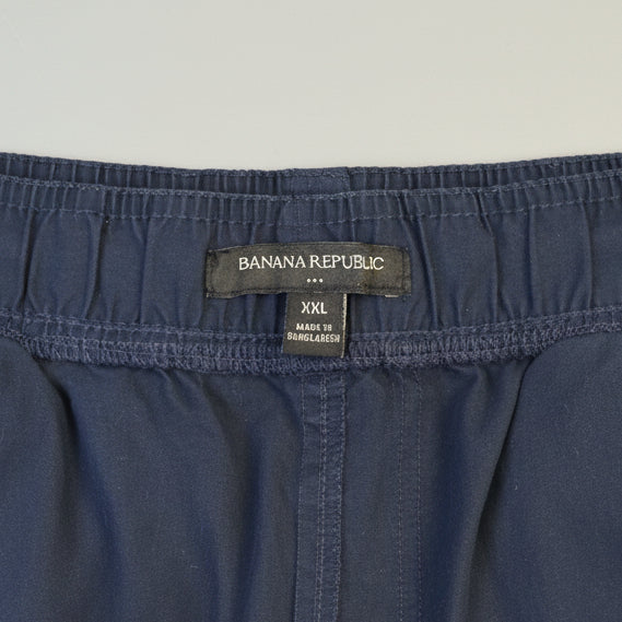 Close-up of the waistband of dark blue denim shorts, showing the brand label 'BAILA NA REPUBLIC' and size 'XXL' on a wooden surface.