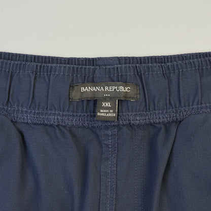 Close-up of the waistband of dark blue denim shorts, showing the brand label 'BAILA NA REPUBLIC' and size 'XXL' on a wooden surface.