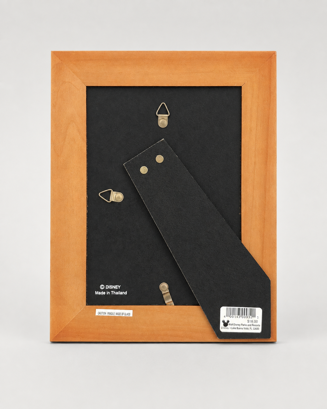 The back of a Disney picture frame with a light wood border, black mounting card, and metal hanging hardware, photographed on a light gray background.