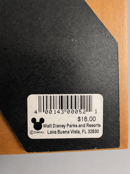 Close-up of the back of a black item showing a white barcode sticker with Disney text and logo, placed on a brown surface.