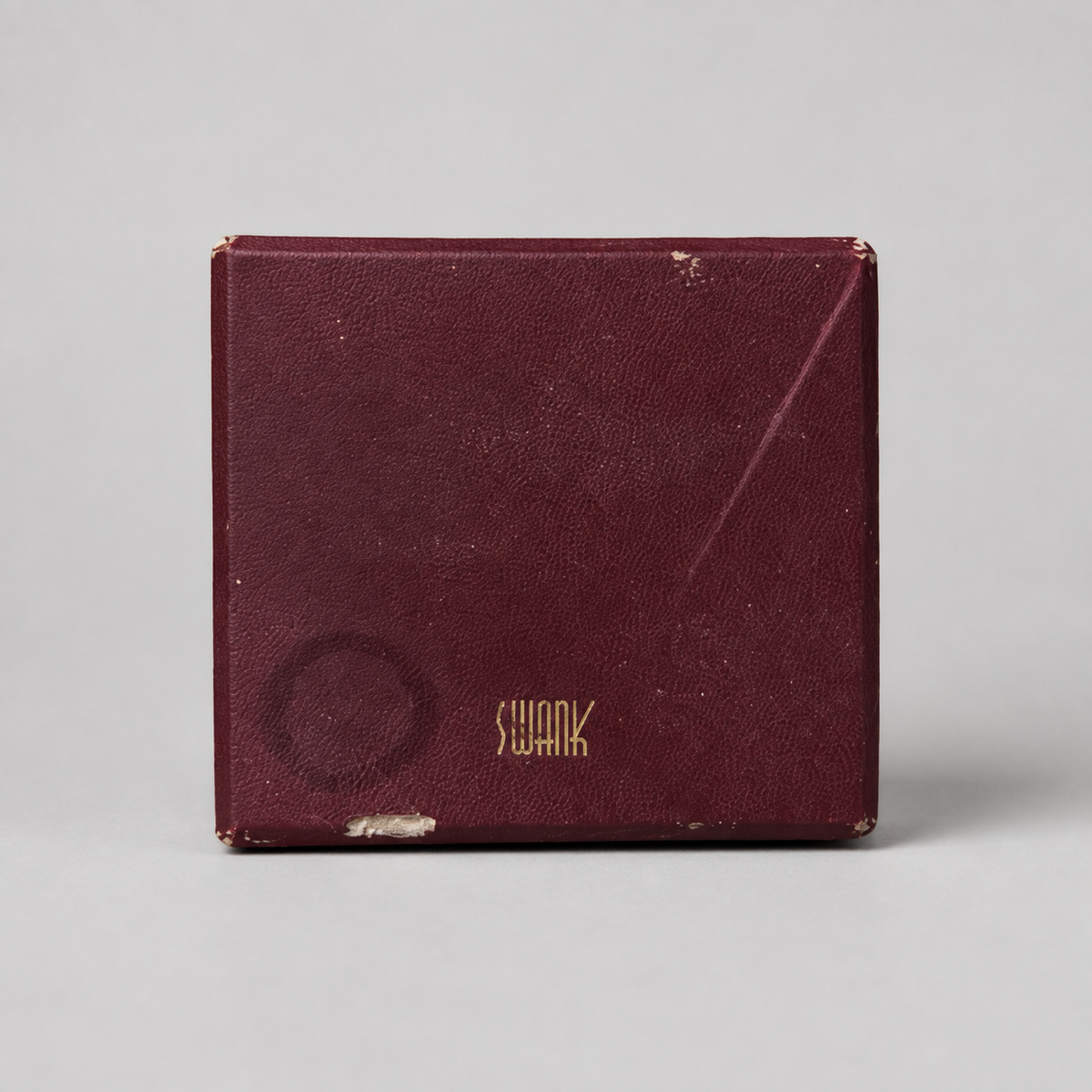A vintage Swank brand burgundy textured leatherette box with gold lettering, shown on a neutral light gray background.