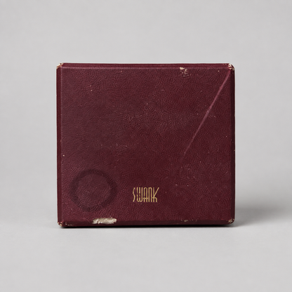 A vintage Swank brand burgundy textured leatherette box with gold lettering, shown on a neutral light gray background.