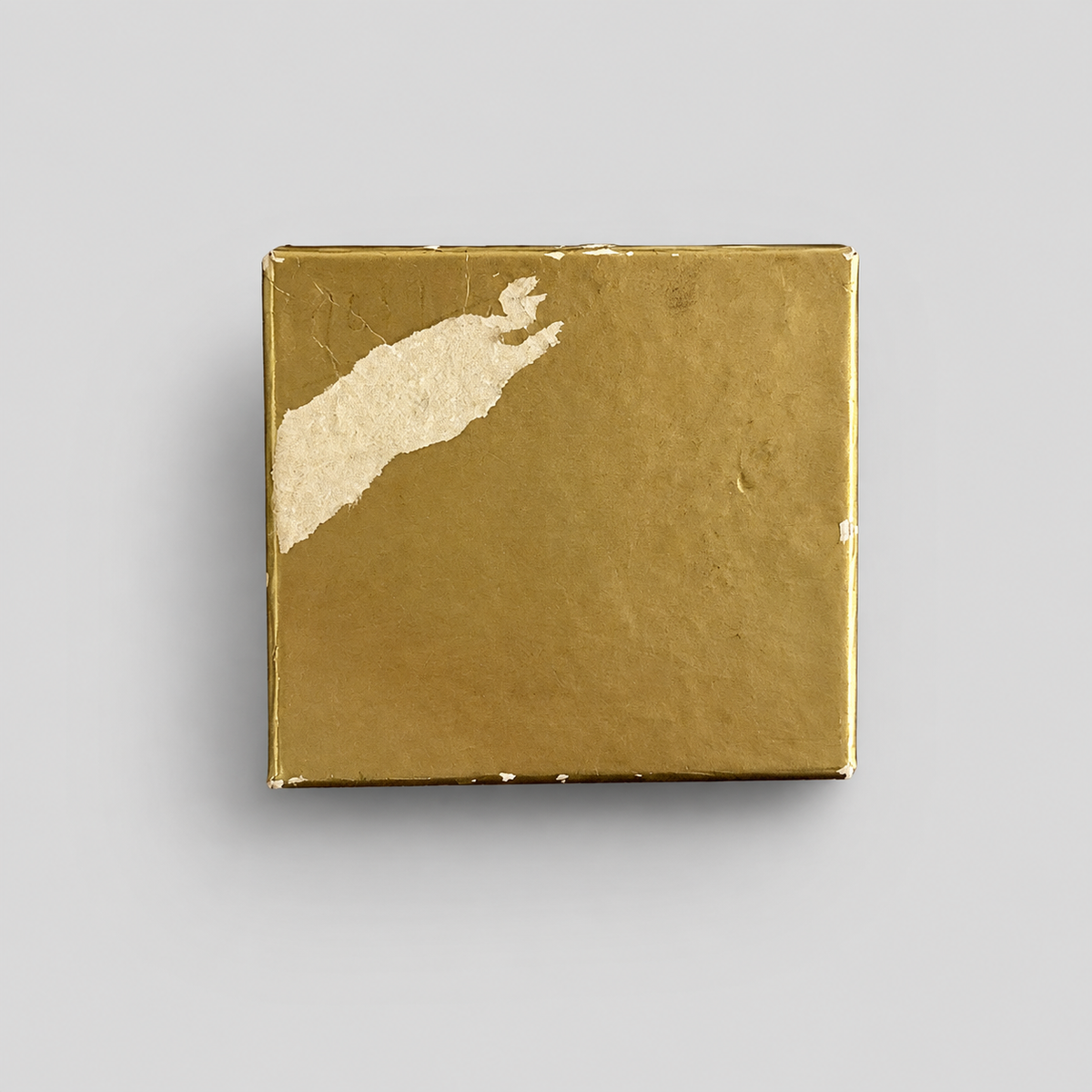 A square gold box with a textured metallic finish and a torn, peeling gold paper accent on the top-left corner, shown on a neutral light gray background.