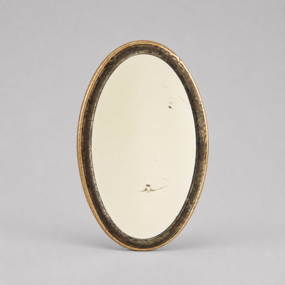 An oval vintage mirror with a distressed gold-toned frame, standing upright against a neutral gray background.
