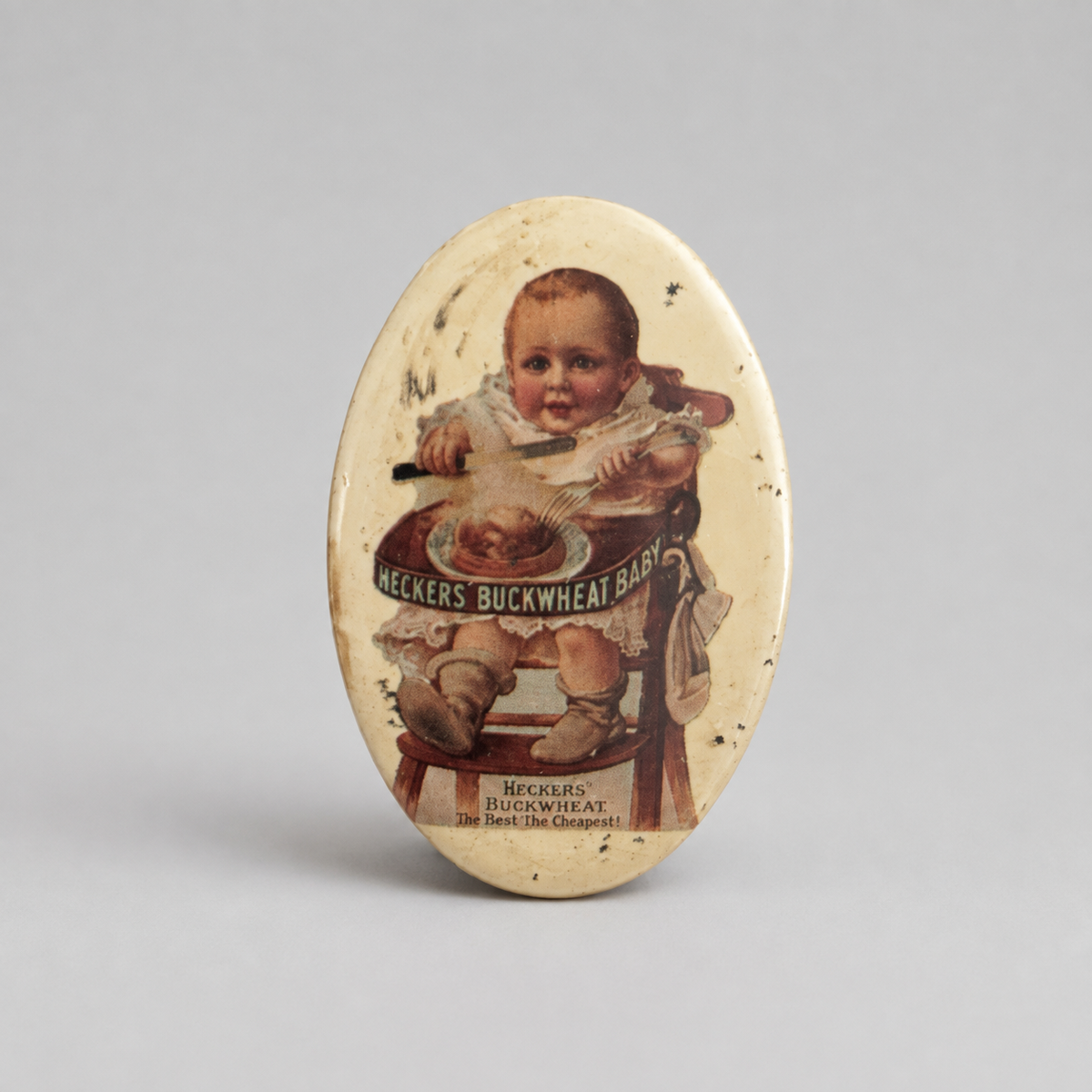 An oval vintage tin sign featuring a printed illustration of a baby in a high chair with the text 'Neckers Buckwheat Baby' and 'Neckers Buckwheat Co.,' shown on a neutral gray background.