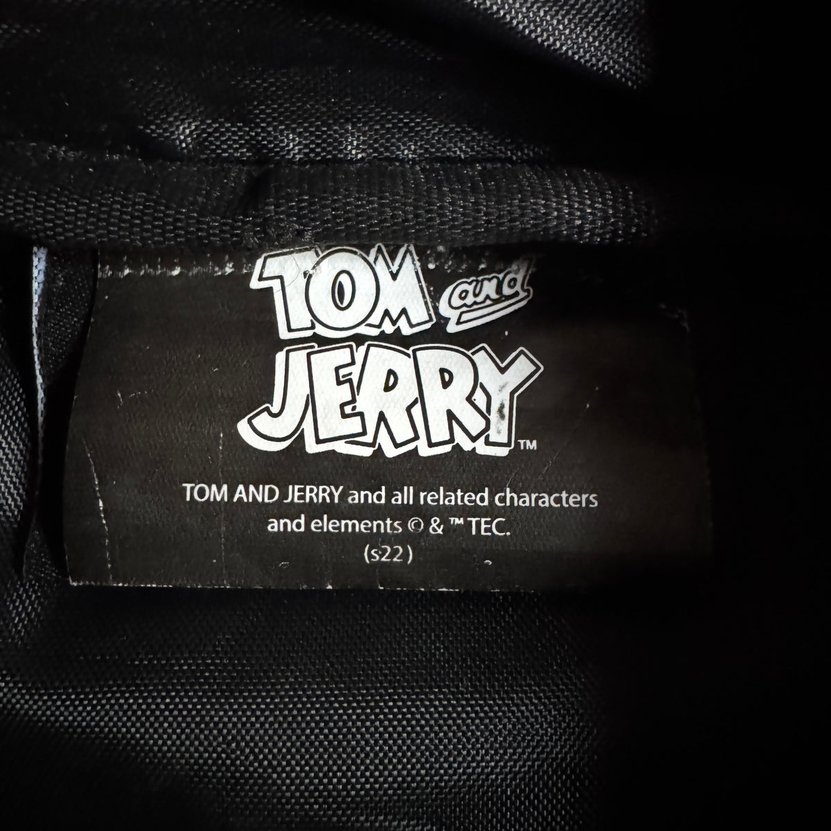 Close-up of a black fabric label with the white 'Tom and Jerry' logo and copyright text sewn onto black woven material.
