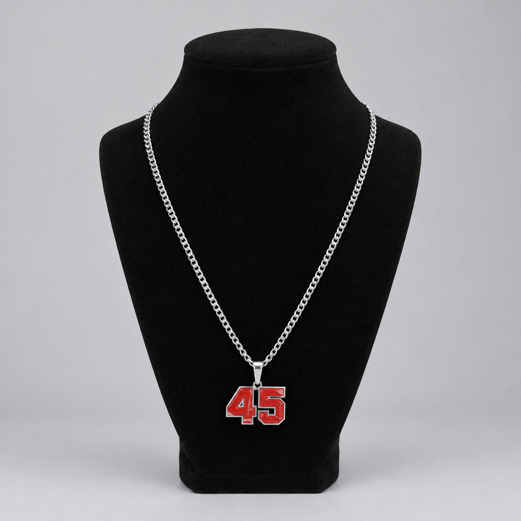 A silver chain necklace with a red and white '45' pendant displayed on a black velvet mannequin bust, set against a home background with a picture frame and small figurines.