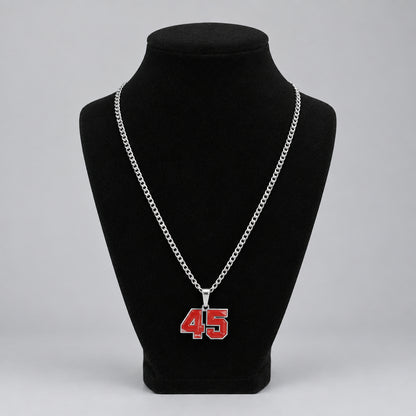 A silver chain necklace with a red and white '45' pendant displayed on a black velvet mannequin bust, set against a home background with a picture frame and small figurines.