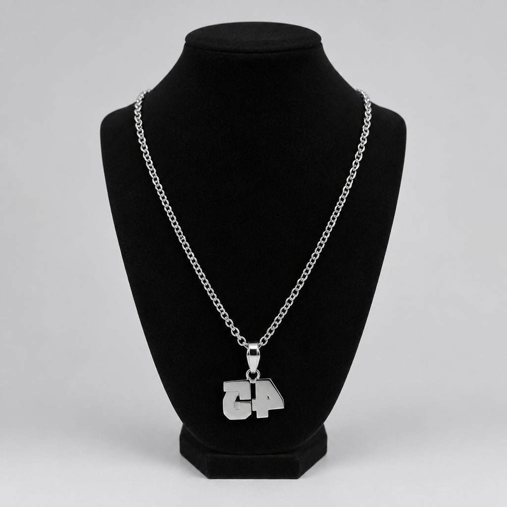 A silver chain necklace with a custom '4' pendant displayed on a black velvet necklace bust, set on a tabletop with blurred background objects.