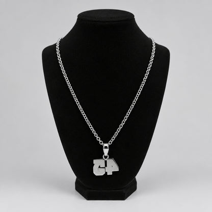 A silver chain necklace with a custom '4' pendant displayed on a black velvet necklace bust, set on a tabletop with blurred background objects.