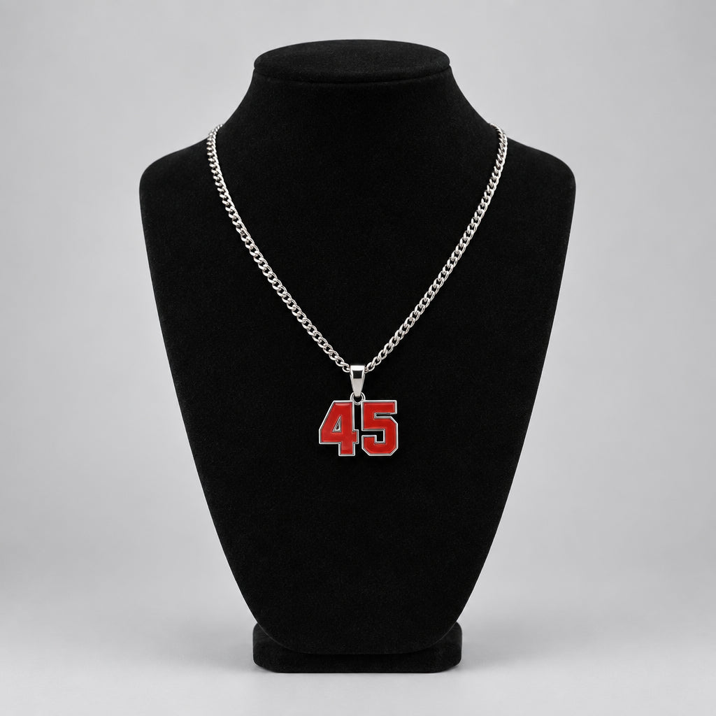 A silver chain necklace with a red and white '45' number pendant displayed on a black velvet mannequin bust. A tattooed hand is visible holding the necklace above the bust.
