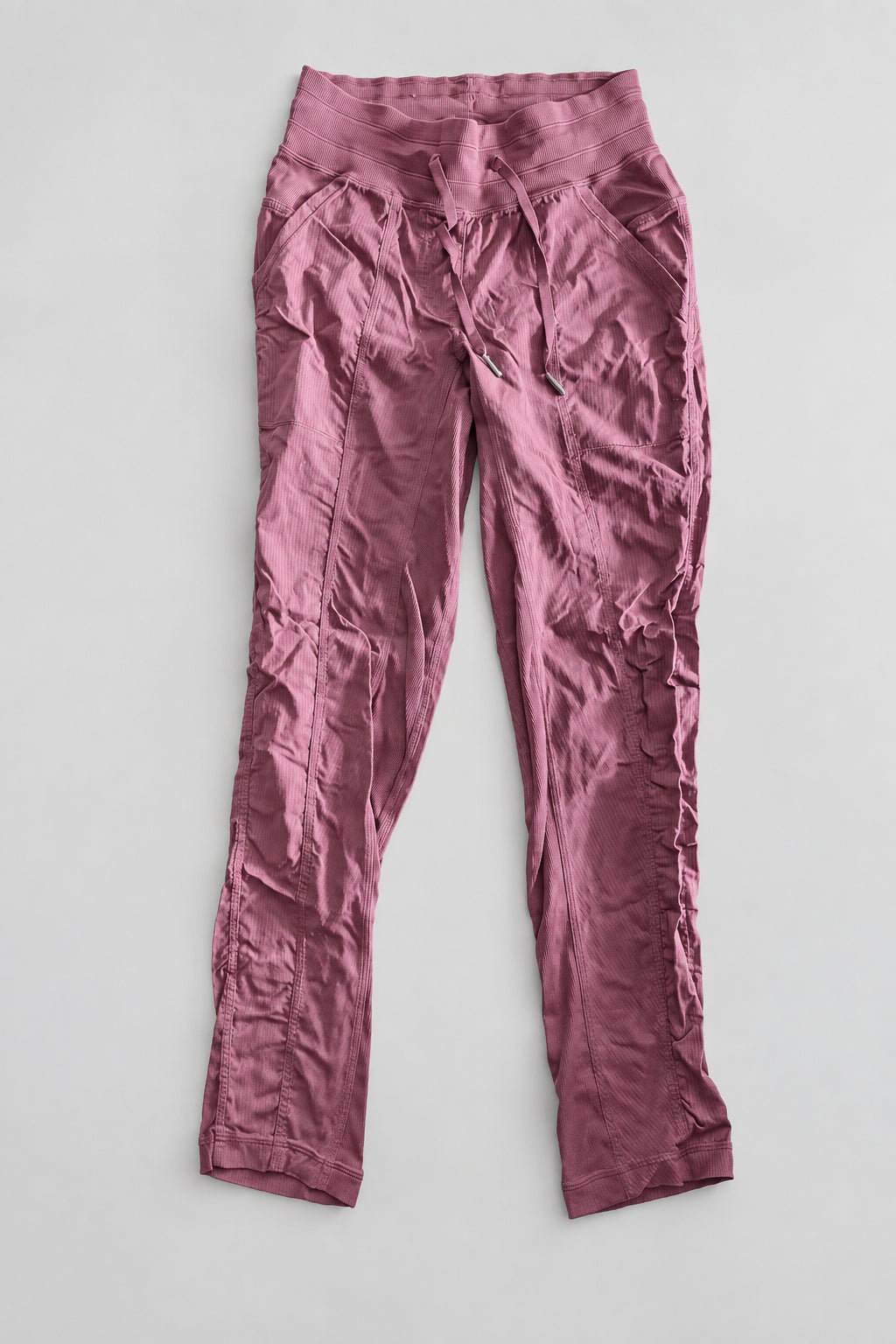 A pair of women's cropped pants in a dusty rose or mauve color, laid flat on a dark wooden table.