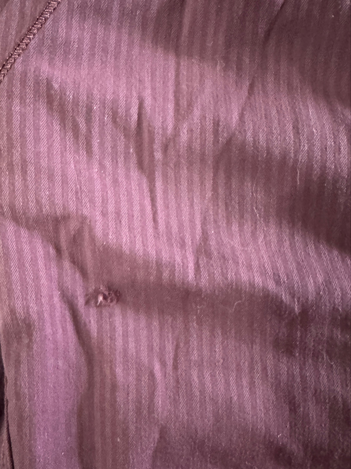 A close-up of a ribbed mauve-purple fabric with visible stitching and a small button detail, laid flat on a dark wooden surface.