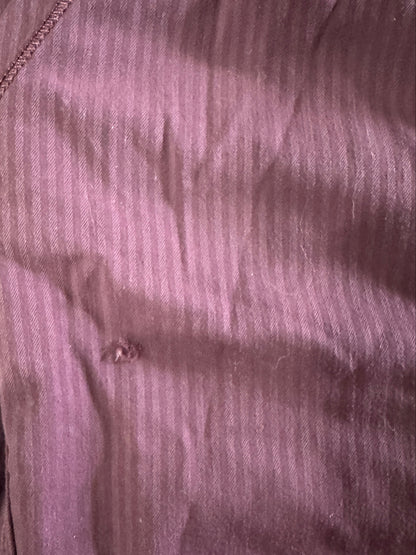 A close-up of a ribbed mauve-purple fabric with visible stitching and a small button detail, laid flat on a dark wooden surface.