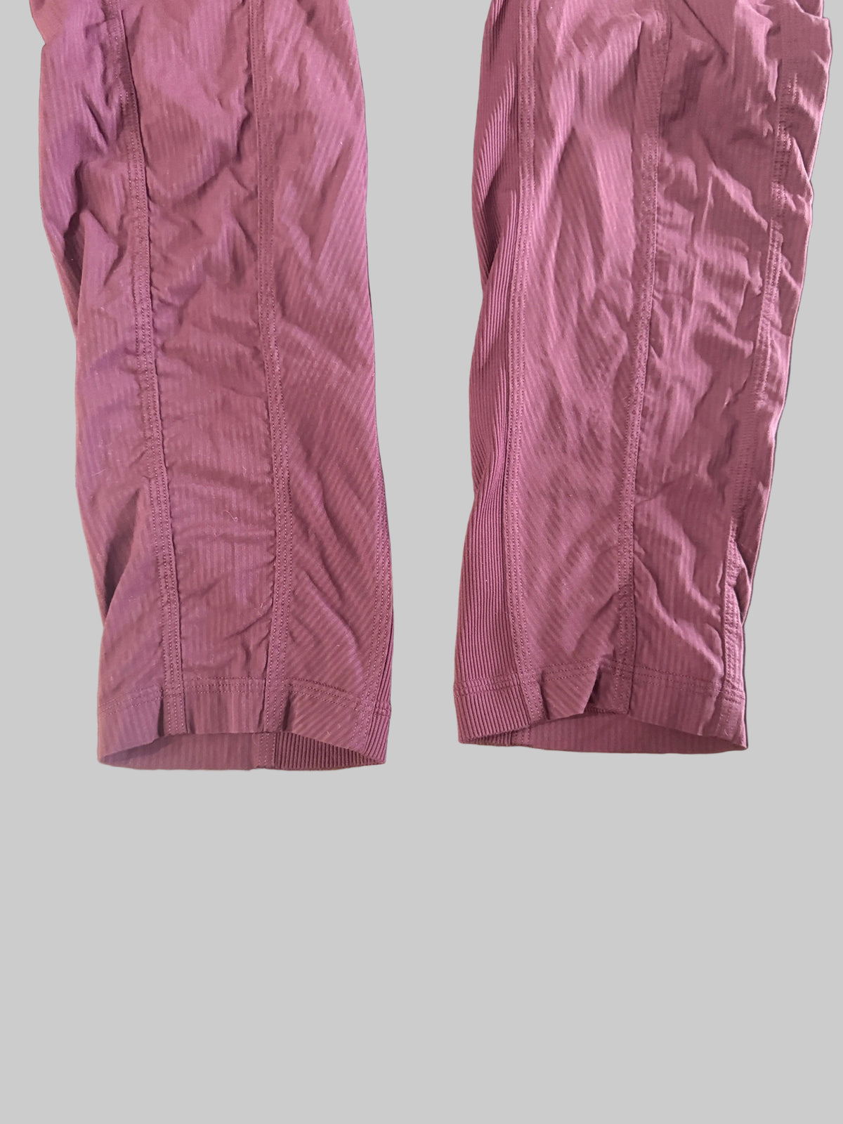 A pair of mauve-colored athletic shorts laid flat on a dark wooden table, with a mirror reflection showing bare feet in the background.