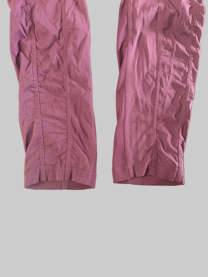 A pair of mauve-colored athletic shorts laid flat on a dark wooden table, with a mirror reflection showing bare feet in the background.