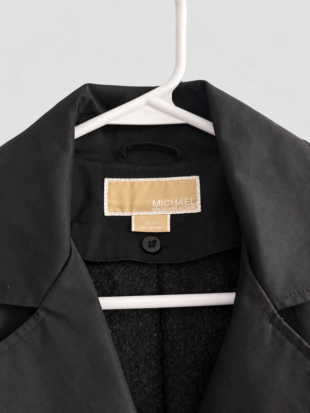 A close-up of a black Michael Kors jacket hanging on a white hanger, showing the interior collar with a tan brand label.