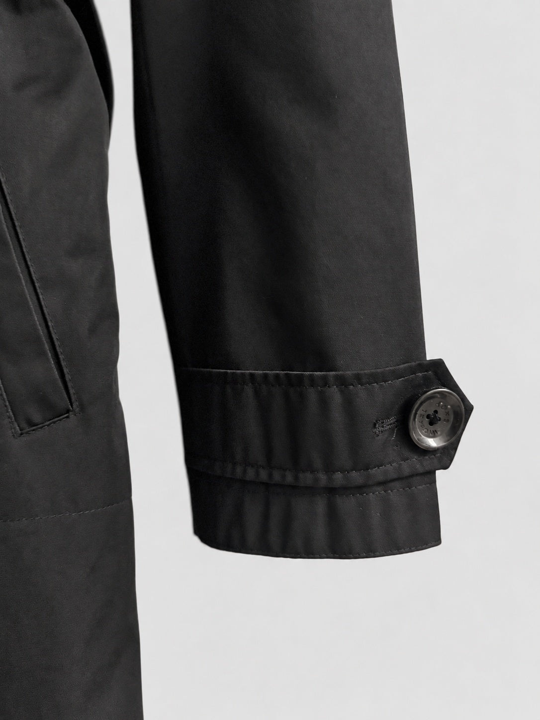 Close-up detail of a black jacket sleeve with a buttoned cuff, shown against a light gray background.