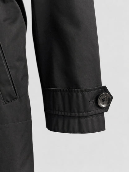 Close-up detail of a black jacket sleeve with a buttoned cuff, shown against a light gray background.
