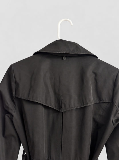 A black trench coat hanging on a white plastic hanger against a light gray background, showing the back view with a button closure and shoulder flap.